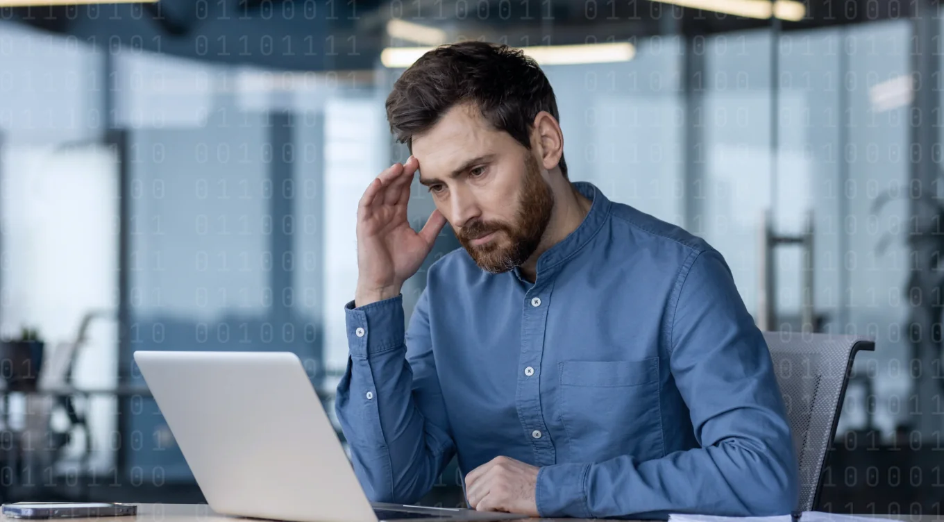 Un uomo con una camicia blu, concentrato sul portatile, mentre lavora alla sua scrivania.
