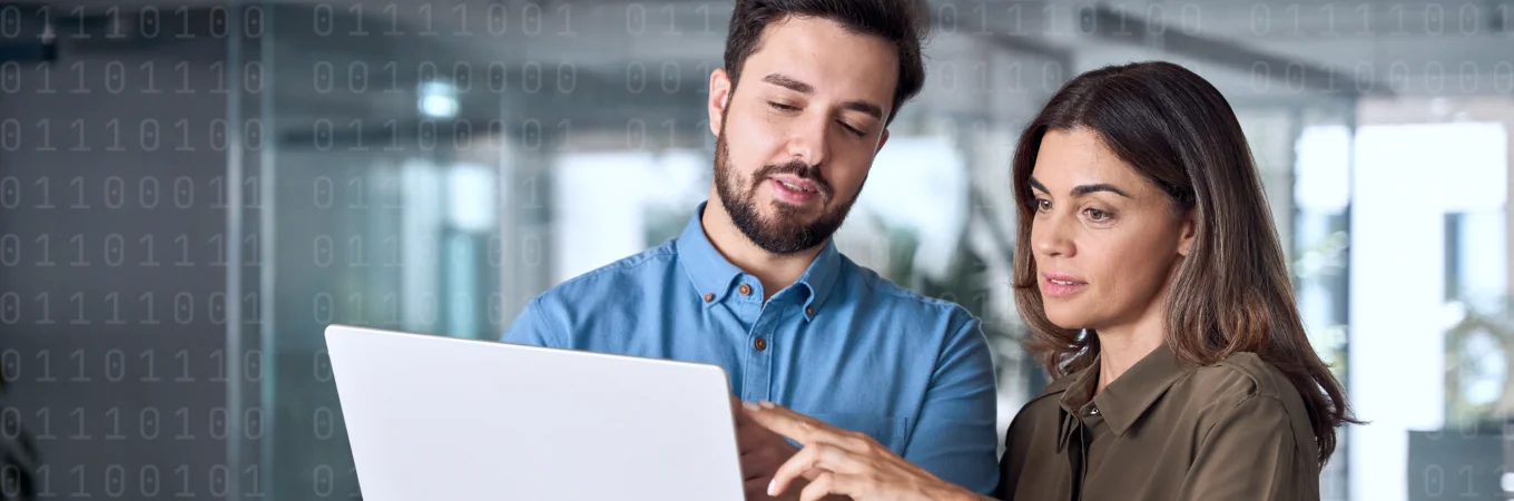 Due persone guardano un computer portatile; un uomo indica qualcosa, con il codice binario sullo sfondo.