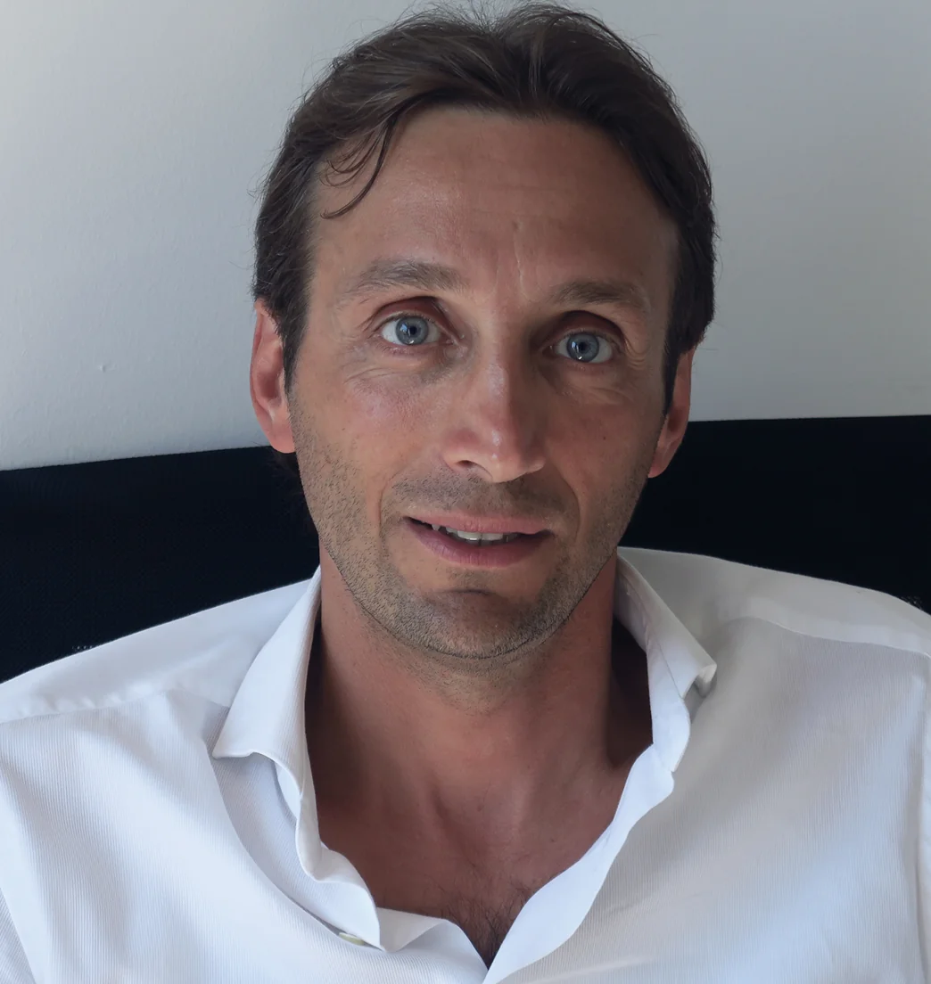 Uomo dalla carnagione chiara, capelli castani e occhi azzurri, in camicia bianca, all’interno di un locale.